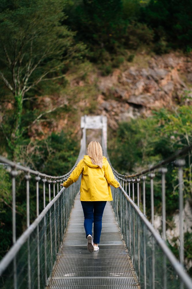 Cheerful female tourist standing on hanging bridge in summer