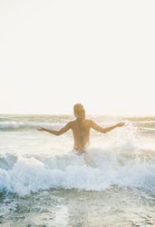 Rear shot of woman in waves at the beach with outstretched arms