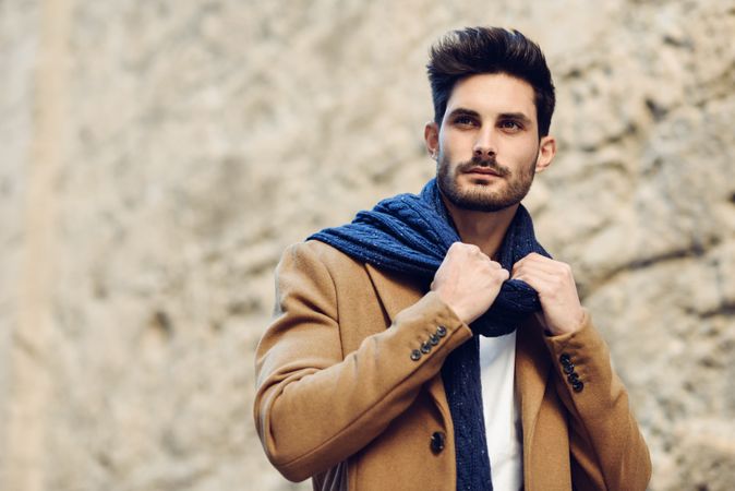 Man in winter coat adjusting scarf walking next to Spanish wall