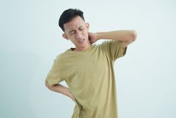 Asian young man touching back of neck and back in pain