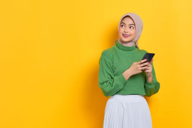 Smiling woman in headscarf looking to the side holding smart phone