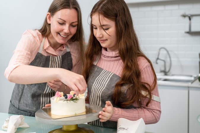 Happy mother and daughter decorating an elegant cake