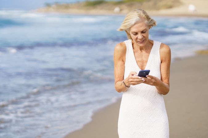 Older female using her smart phone on a rocky beach