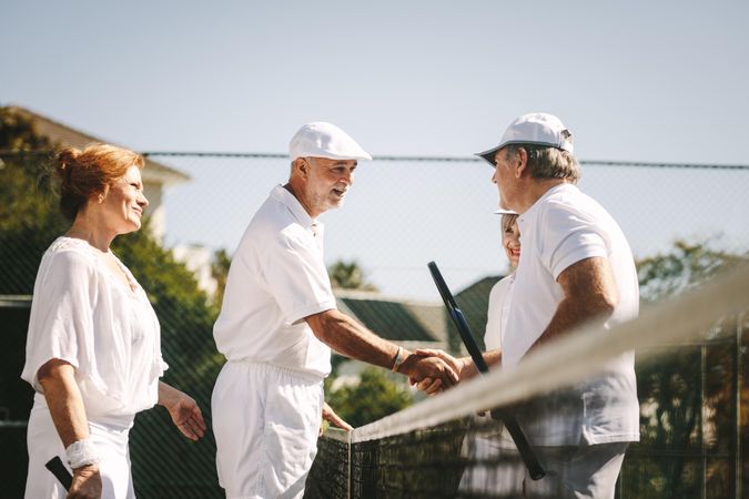 Mature men shaking hands standing on tennis court after the match