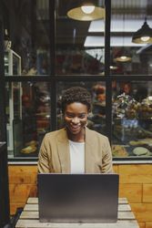 Smiling Black woman sitting at table with laptop in cafe