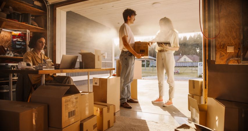 Male Manager Using Laptop To Fill Online Orders, Hispanic Female Co-Founder With Tablet Talking To Man Responsible For Shipping.