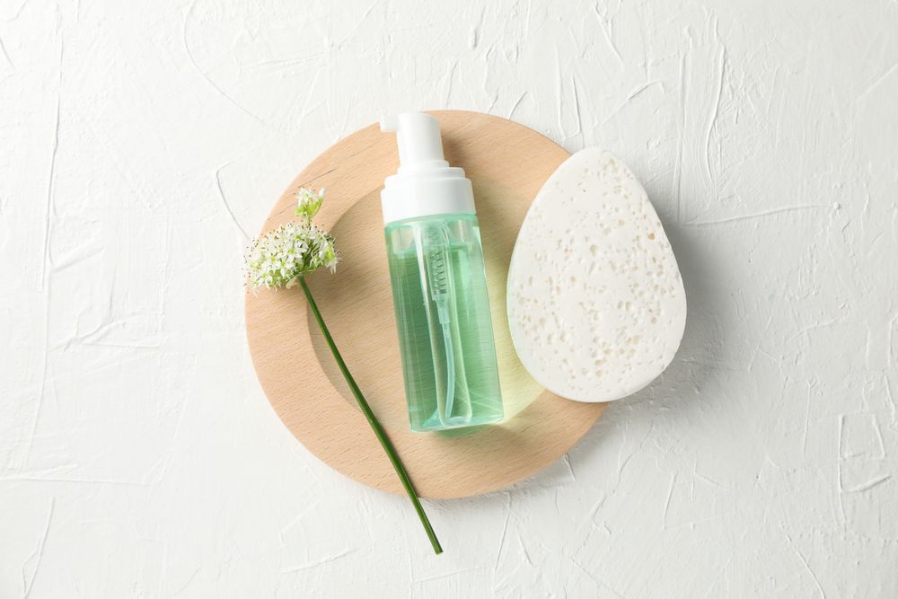 Lotion, allium flower and sponge on blank background, copy space