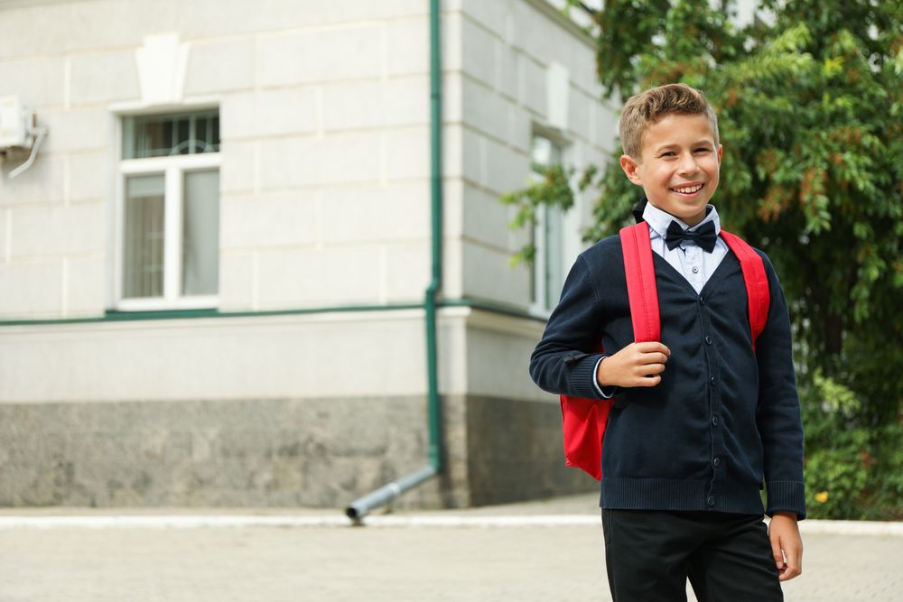Boy with backpack against school building, space for text