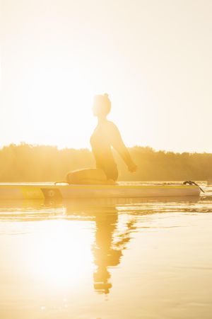 Woman stretching her arms on paddleboard in the sunrise