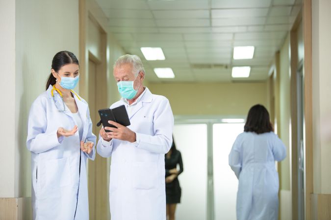 Doctors wearing protective mask discussing and consulting patient case over a smart phone