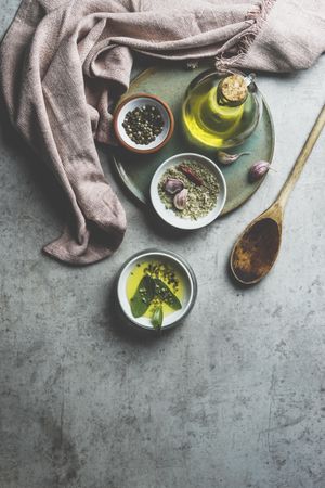 Healthy cooking ingredients on grey concrete kitchen table: olive oil, sage, garlic, pepper, salt, wooden cooking spoon, dish cloth