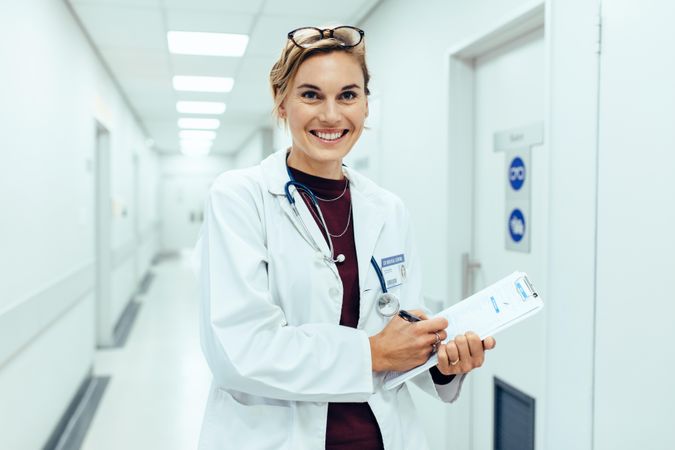 Portrait of happy young female doctor standing in hospital corridor