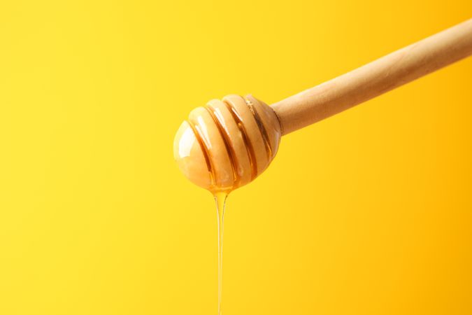 Dipper with honey on yellow background, space for text