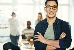 Portrait of Asian man smiling with arms crossed in bright office