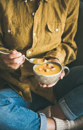 Woman in jeans eating cup of squash soup