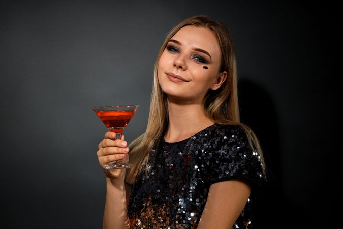 A woman at a party in the style of Halloween with a cocktail in her hands
