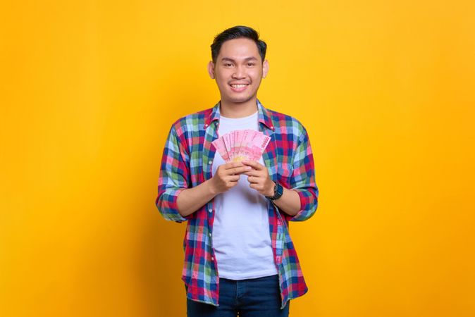 Smiling Asian man holding up cash in studio shoot