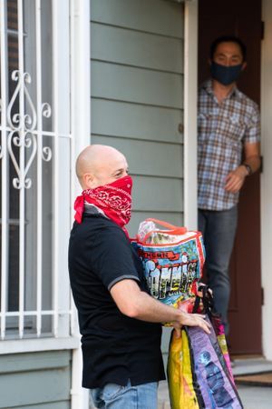 Man delivering bags of groceries to a man waiting at his front door