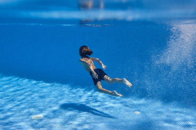 Unrecognizable barefoot boy swimming in blue pool