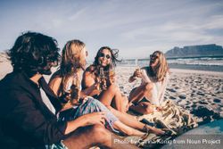 Smiling group of friends sitting on the beach enjoying drinks A0yqa0