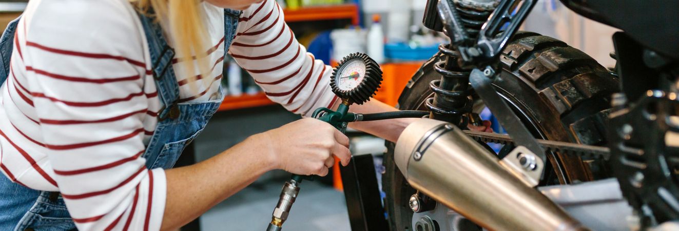 Mechanic woman checking tire air pressure of motorcycle