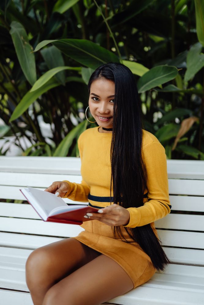 Graceful long haired Asian woman reading book on bench in park