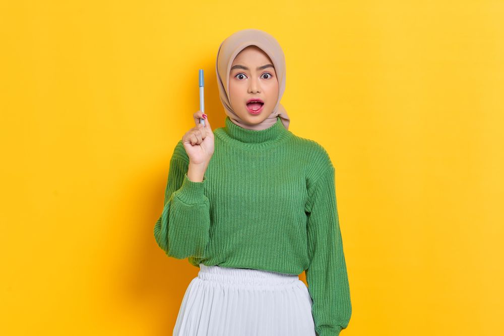 Surprised woman in headscarf holding up pen