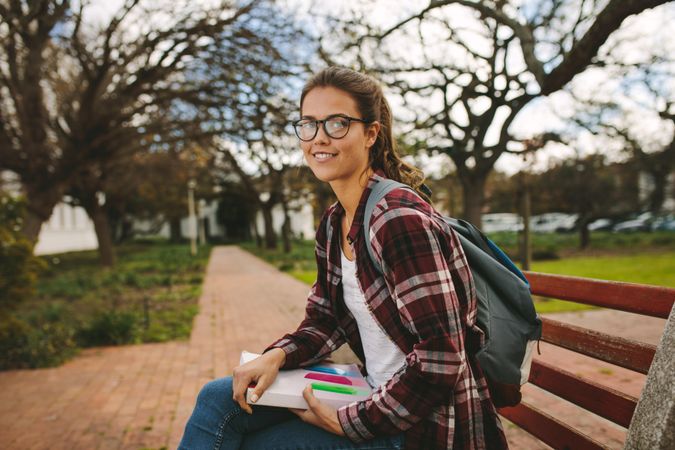 Beautiful female student sitting on bench with book