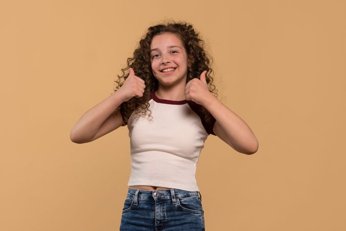 Cheerful young girl giving double thumbs-up, smiling brightly