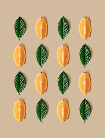 Pattern of green leaves and orange slices on  pastel sand background