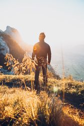 Back view silhouette of a man standing on brown grass in mountains 42x7q0