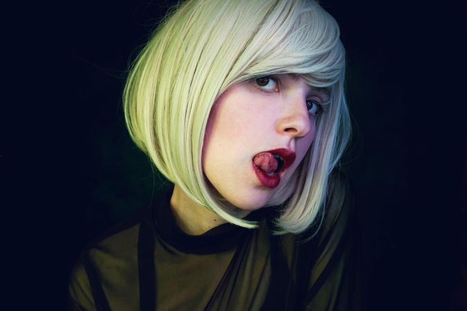 Portrait of woman with blonde short hair and red lipsticks against dark background