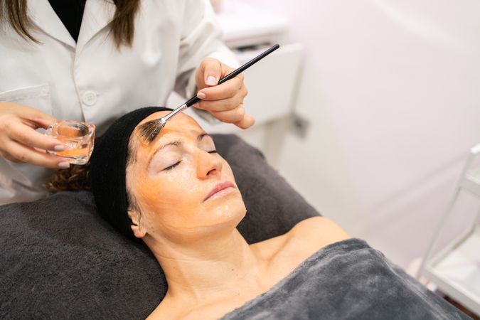 Professional beautician spreading treatment on face of female client