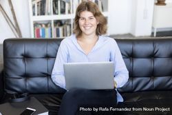 Content woman sitting on a sofa at home working on a laptop 0yXPDn