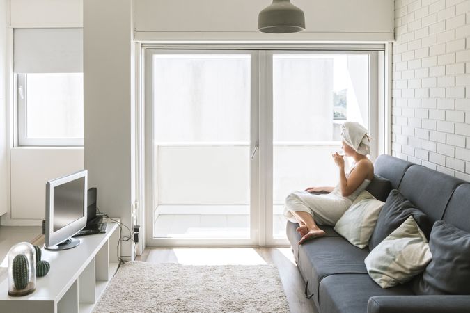 Adult relaxed woman enjoying life while resting on sofa and having hot drink after shower in own cozy apartment