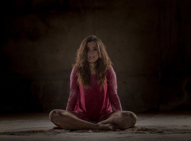 Young woman in lotus pose between sand in darkness