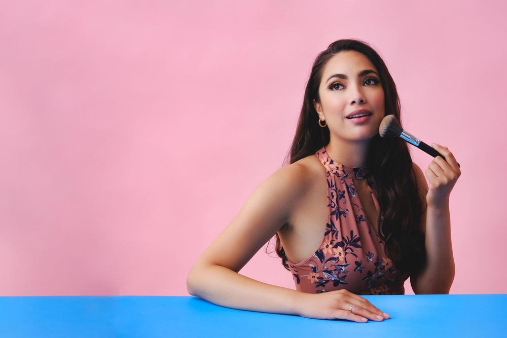 Hispanic woman with long brown hair holding large make up brush, copy space