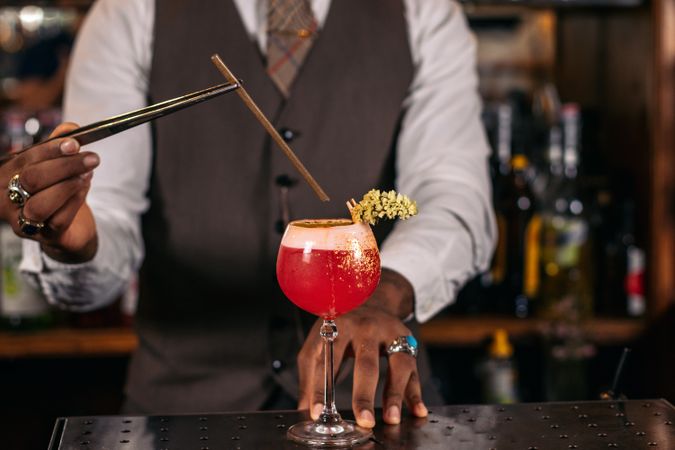 Close-up of an unrecognizable Black bartender pouring a cocktail and decorating it with garnish