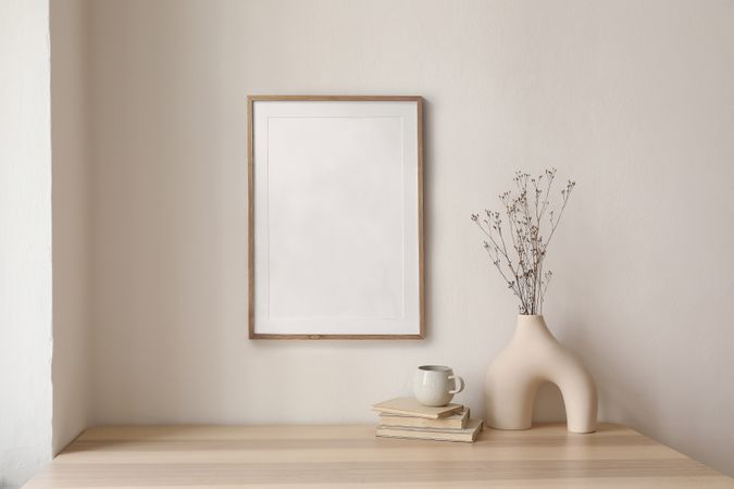 Modernist vase and decorative reeds, and coffee atop pile of books with blank frame