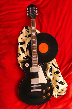 Vinyl record and electric guitar on bed