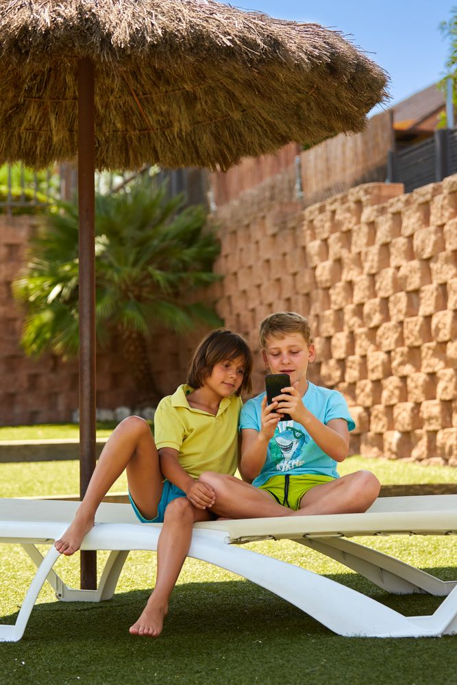 Cheerful boys browsing smartphone on sunbed