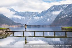 Woman stretching her arms out standing on a bridge over alpine lake bYM81b