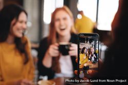 Woman taking photo of her friends with her smart phone at a coffee shop 5wpj64