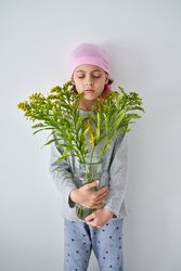 Serene kid in bandana with goldenrods in vase near wall