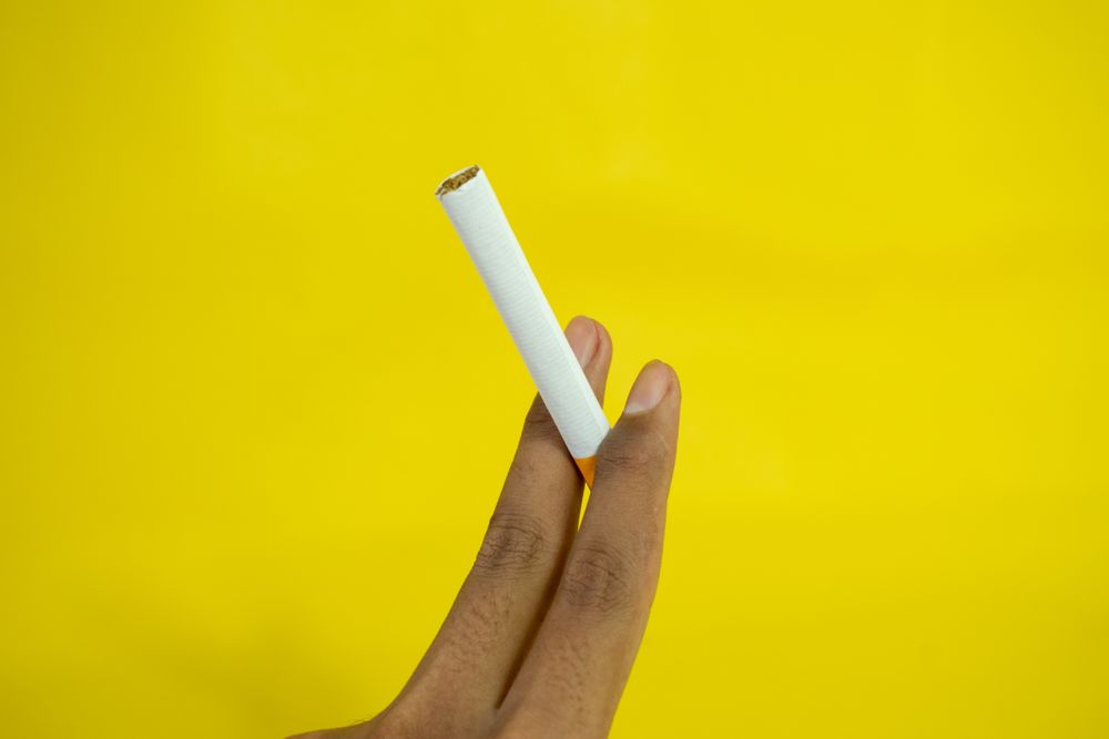 Hand holding cigarette against yellow wall
