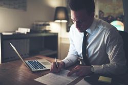 Man in shirt and tie working on documents late at night at his desk