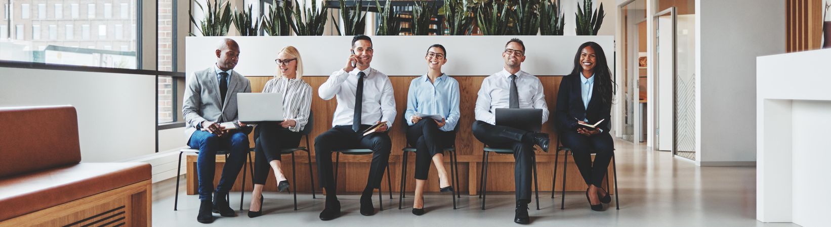 Group of people sitting and smiling in a row in a bright office, wide shot