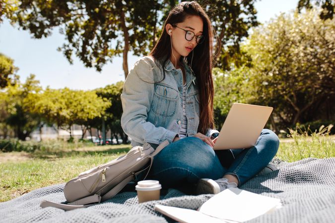 Young college student working on laptop sitting in a park listening to music
