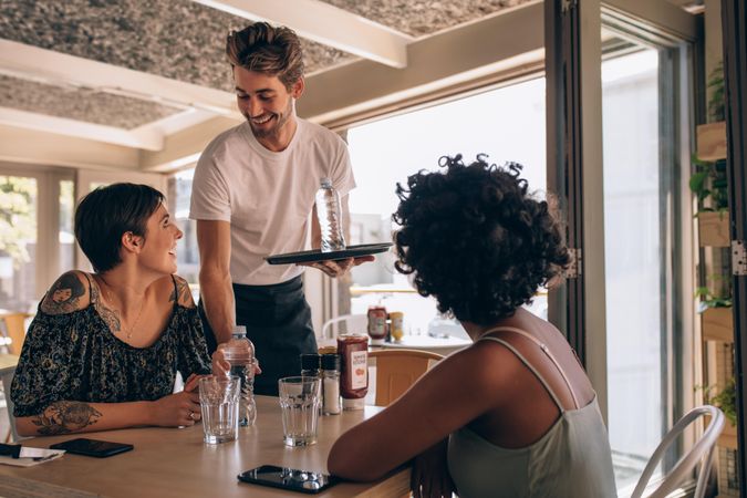 Male waiter serving water to women at cafe