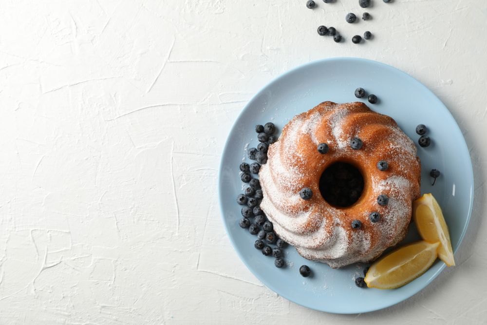 Cake with powdered sugar, blueberry and lemon on plain background, copy space